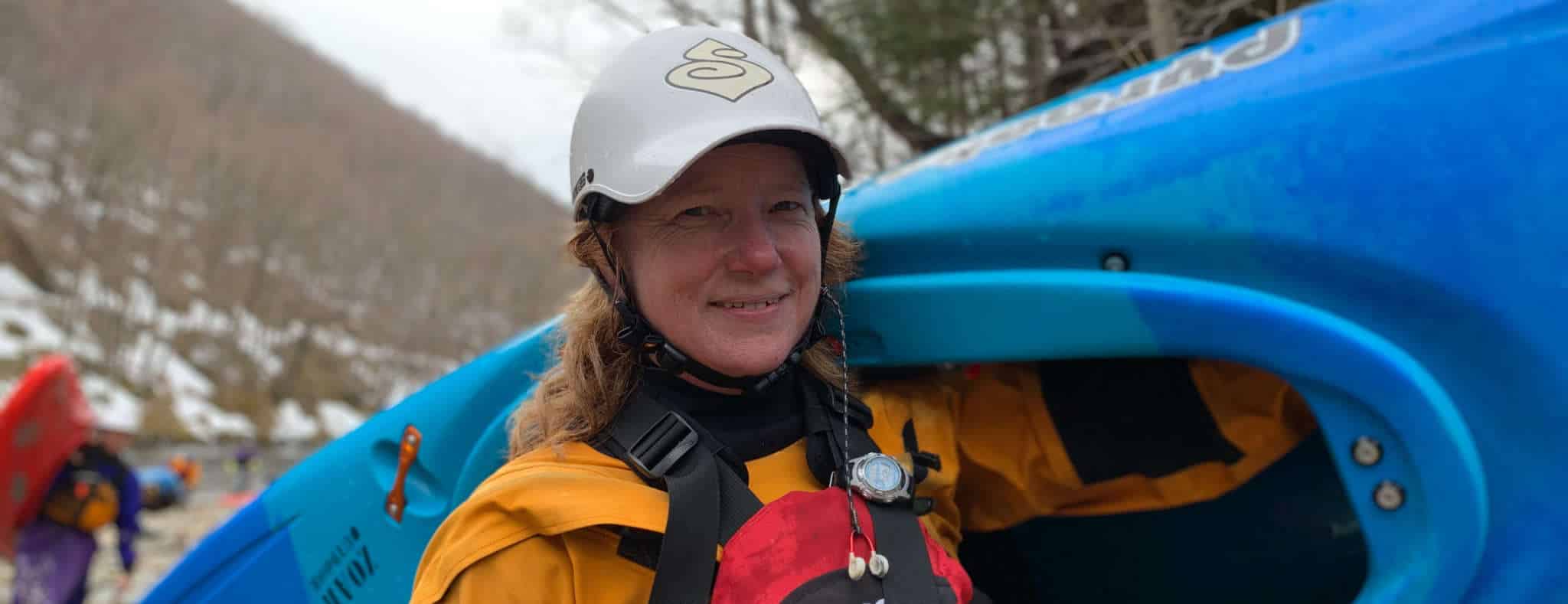 woman carrying kayak on shoulder along river