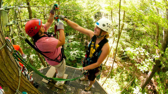 Zip-lining instructor helping a woman buckle in for a zip