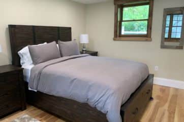 Queen bed with grey bedspread in bedroom with windows