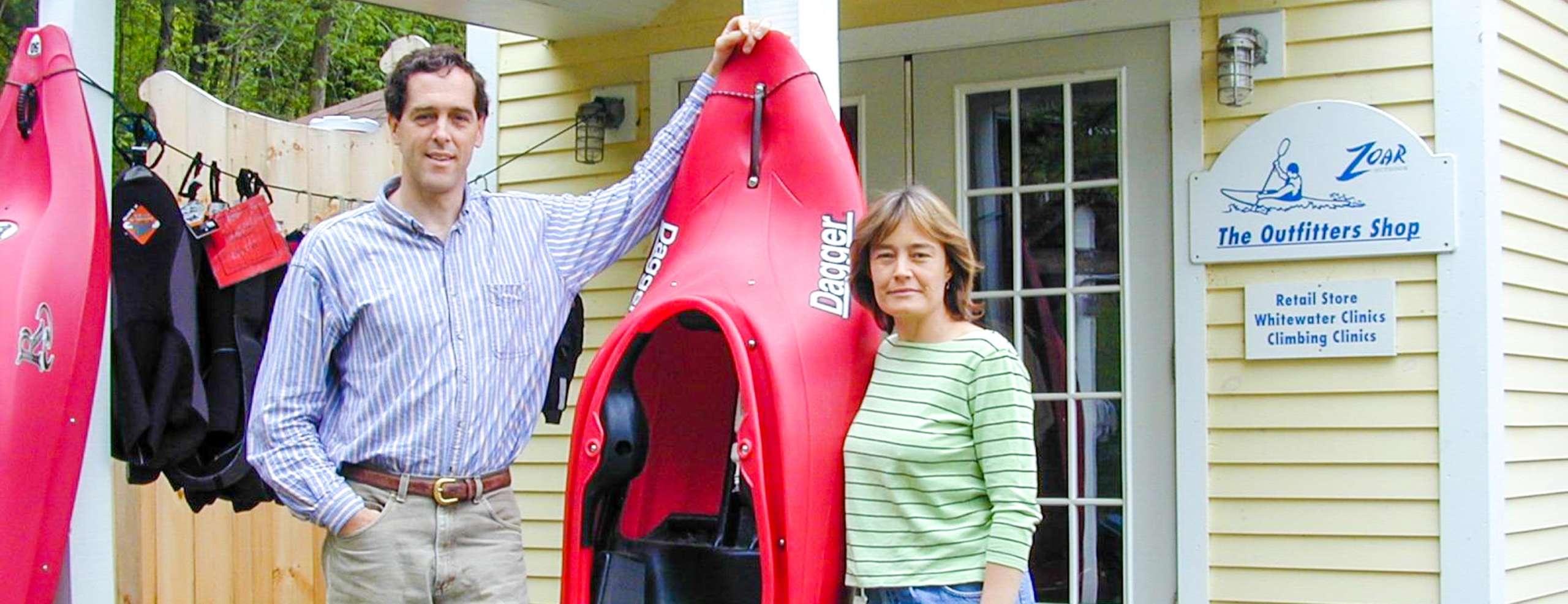 Founders Bruce and Karen standing by a kayak perched up against a house
