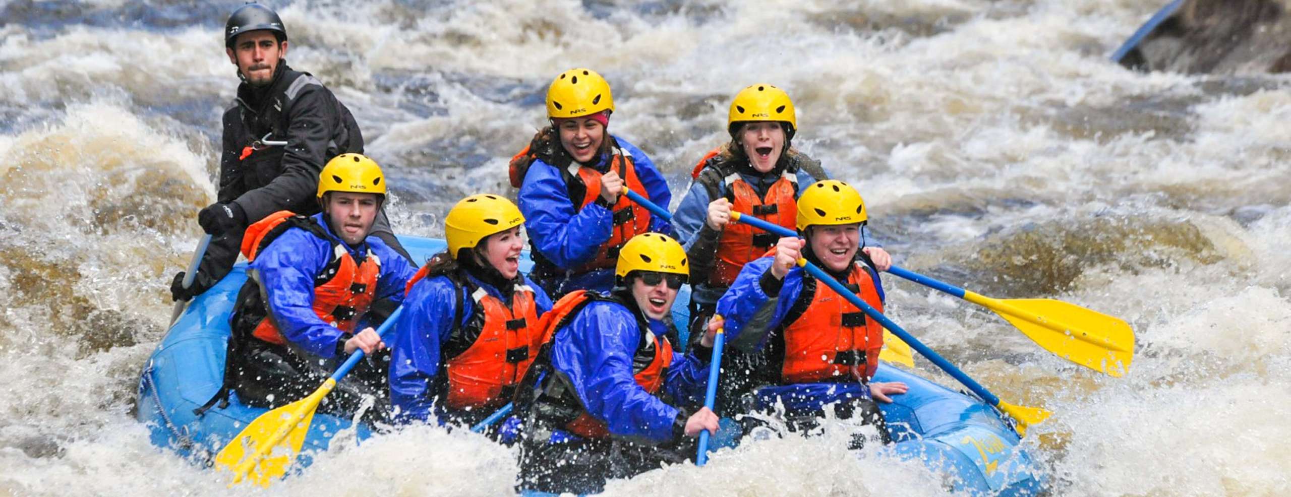 Group of people in a raft paddling during rapids