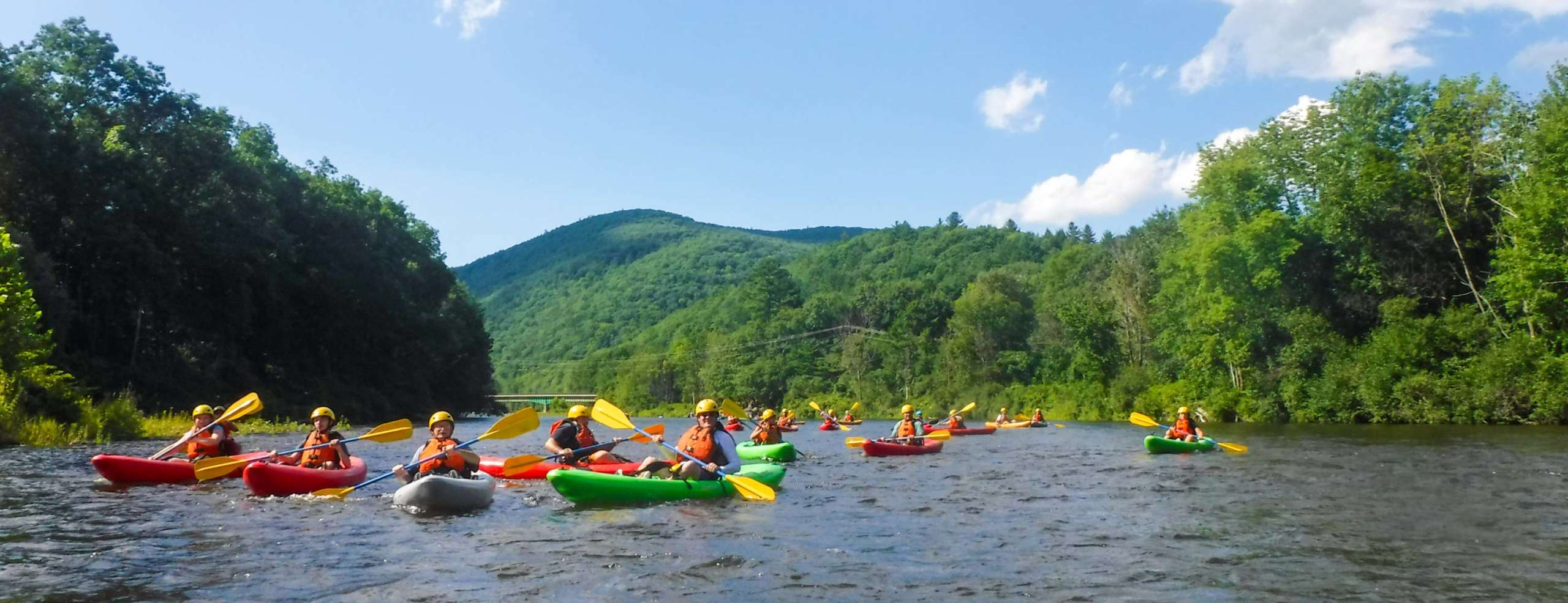 Group of kayakers on a calm river with green mountains in background