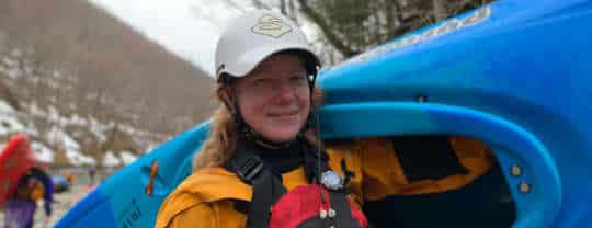 Janet holding her kayak on the river bank
