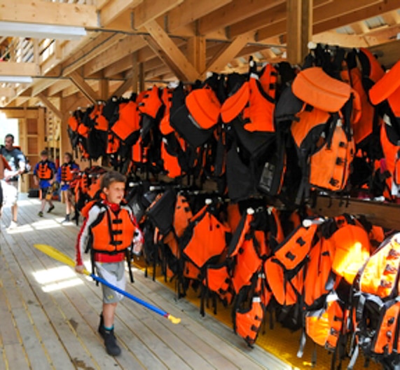 Child walking by all of the hanging life vests in equipment barn
