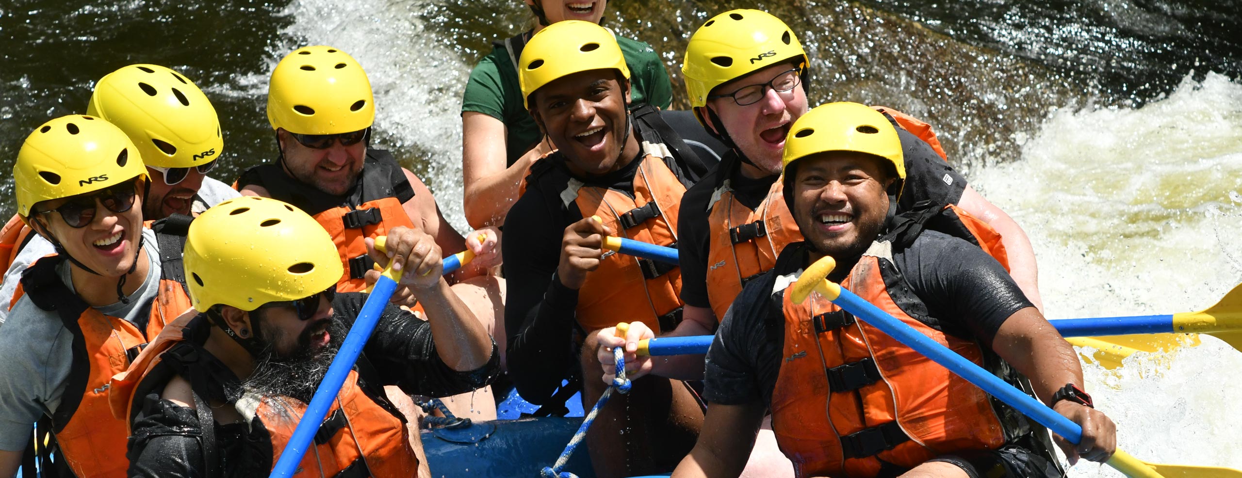 Group of people in a raft smiling and having fun paddling