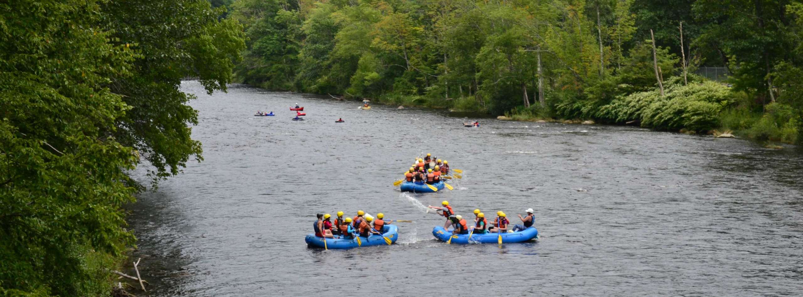 Three rafts floating down a river with rafters splashing each other with water