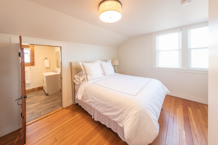 Bright white bedroom with hardwood floors and queen bed and attached bathroom