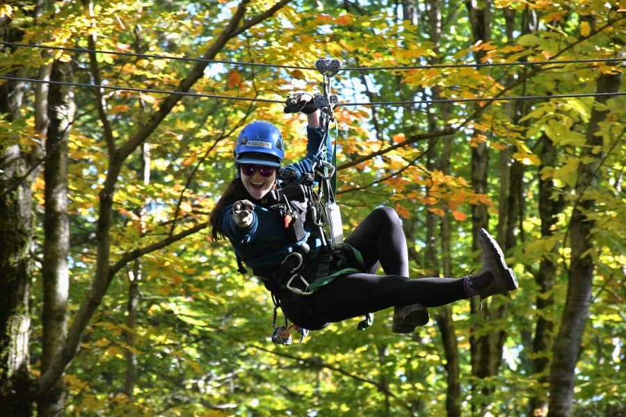 Smiling zipliner flying through the trees pointing at the camera